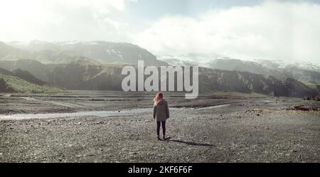 Eine Frau, die in Thorsmork im isländischen Hochland auf einer offenen Ebene mit Bergen in der Ferne steht Stockfoto
