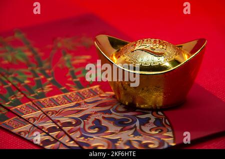 Chinesische Neujahrspakete mit chinesischen Goldbarren auf rotem Hintergrund. Anpassbarer Platz für Text. Stockfoto