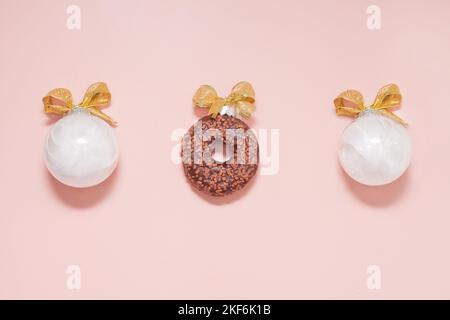 Weiße weihnachtskugeln mit Donut und goldenen Schleifen. Neujahr kreative Dekoration auf rosa Hintergrund Stockfoto