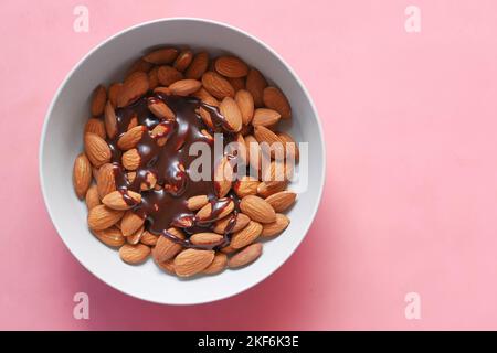 Dunkle Schokoladencreme, die in einer Schale auf Rosa auf Mandelnüsse gießt Stockfoto