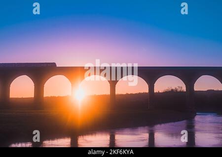 Farbenfrohe Luftaufnahme des Sonnenaufgangs mit dem Zug auf dem Arthington Viaduct, Großbritannien Stockfoto