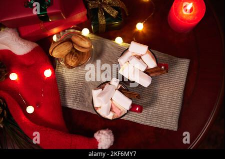 Stillleben. Becher mit heißem Schokoladengetränk mit Marschmalchen und Zimt, auf festlichem Weihnachtstisch vor verschwommenem Hintergrund brennbarer Kerzen, Xma Stockfoto