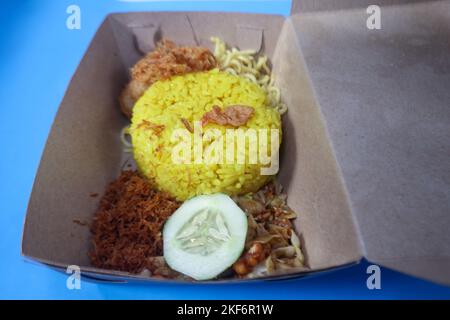 Indonesische traditionelle Gerichte, nämlich gelber Reis mit gebratener geriebener Kokosnuss, einfache Nudeln, Kartoffelkuchen, getrocknete Tempeh und eine Scheibe Gurke. Stockfoto