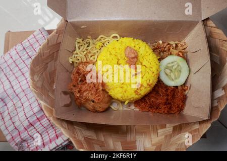 Ein Blick von oben auf traditionelle indonesische Speisen, nämlich gelber Reis mit gebratener geriebener Kokosnuss, einfache Nudeln, Kartoffelkuchen, getrocknete Tempeh und eine Scheibe Stockfoto