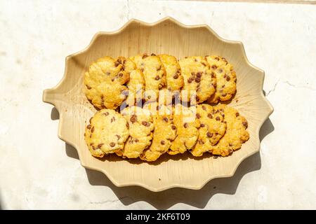 Kekse gebacken mit Schokoladenstückchen. Direkt über der Makrofotografie einer Platte mit Blick auf die frischen Kekse mit direktem Sonnenlicht und shado Stockfoto