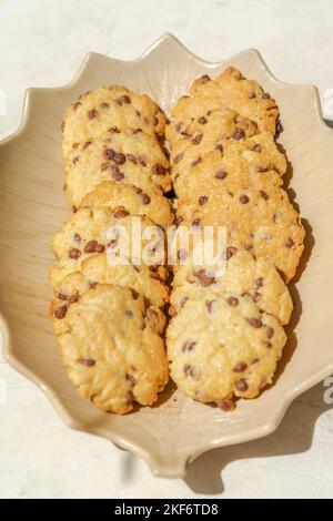 Kekse gebacken mit Schokoladenstückchen. Direkt über der Makrofotografie einer Platte mit Blick auf die frischen Kekse mit direktem Sonnenlicht und shado Stockfoto