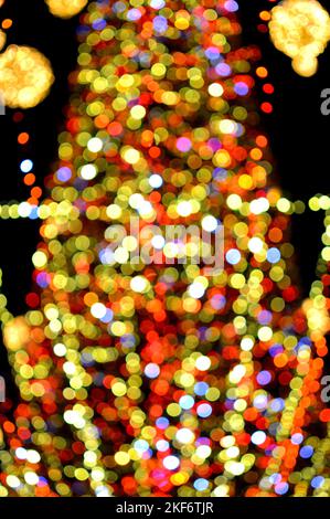 Unscharfer Hintergrund. Schöne leuchtende und blinkende Neujahr und Weihnachtsdekoration Girlanden und glühende Kugeln für Weihnachtsbaum hängen im Freien in schwarzer Nacht.verschwommen blinkende Bokeh Flecken Hintergrund Stockfoto