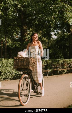 Hübsche junge Frau mit weißem bichon Frisehund im Korb mit Elektrofahrrad Stockfoto