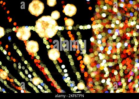 Unscharfer Hintergrund. Schöne leuchtende und blinkende Neujahr und Weihnachtsdekoration Girlanden und glühende Kugeln für Weihnachtsbaum hängen im Freien in schwarzer Nacht.verschwommen blinkende Bokeh Flecken Hintergrund Stockfoto