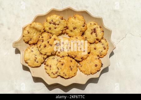 Kekse gebacken mit Schokoladenstückchen. Direkt über der Makrofotografie einer Platte mit Blick auf die frischen Kekse mit direktem Sonnenlicht und shado Stockfoto