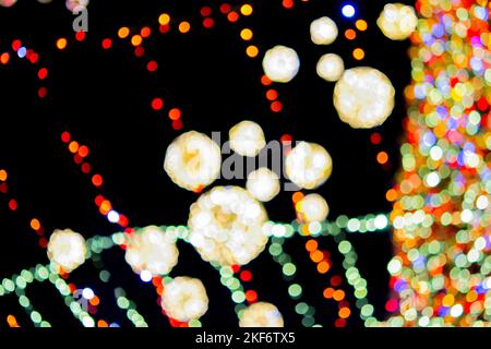 Unscharfer Hintergrund. Schöne leuchtende und blinkende Neujahr und Weihnachtsdekoration Girlanden und glühende Kugeln für Weihnachtsbaum hängen im Freien in schwarzer Nacht.verschwommen blinkende Bokeh Flecken Hintergrund Stockfoto