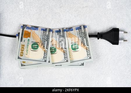 Schwarzer Stecker und viele 100-Dollar-Banknoten auf dem Stromkabel. Steigende Strompreise in der Welt. Hohe Energiekosten, Weltenergie und po Stockfoto