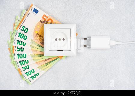 Weiße Steckdose mit Stecker mit vielen Euro-Banknoten auf hellem Hintergrund. Konzept der steigenden Strompreise in Europa. Hohe Energiekosten, weltweit Stockfoto