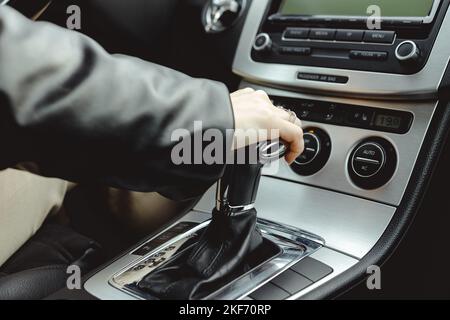 Der Fahrer hält am Schalthebel des Automatikgetriebes fest. Eine Frau wechselt in einem Auto den Gang. Stockfoto