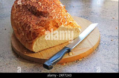 Ungeschnittener frischer Laib Brot auf einem Brotbrett mit einem Schneidemesser, fertig zum Schneiden. Stockfoto