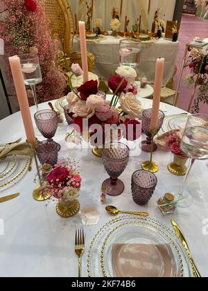 Festliche Tischkulisse in pink-violett-rotem Stil mit Kerzen und Blumen. Stockfoto