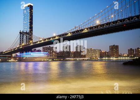 Eine lange Exposition von Transportmitteln, die am Abend unter der Brooklyn Bridge, New York, vorbeifahren Stockfoto