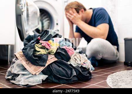 Müde und unglücklich von Wäsche, Wäsche waschen, Hausarbeiten und Hausarbeit. Trauriger Mann oder überfordert junger Vater. Waschmaschine defekt. Stress bei der Elternschaft. Stockfoto