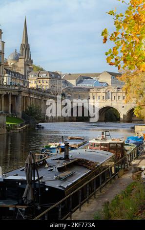 Kanalboote, Hausboote, die auf dem Fluss Avon über das Weir zur Pulteney Bridge und zum Stadtzentrum von Bath im Herbst in Bath, Großbritannien, festgemacht sind Stockfoto