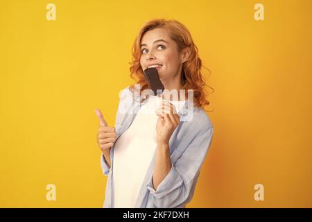 Junge Frau isst leckeres Eis, genießt gefrorenes Dessert, in legerer Kleidung gekleidet, isoliert auf gelbem Hintergrund. Stockfoto