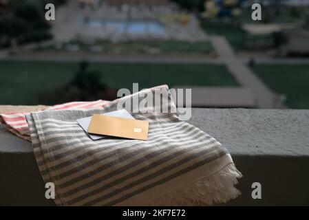 Goldene und weiße Bankkarte auf Strandtuch auf dem Hintergrund des Hotelpools in Moraitika, Korfu, Griechenland. Das Konzept Der Zahlung Für Entspannung Und Stockfoto