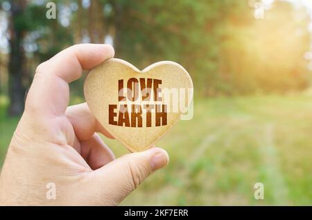Ökologisches Konzept. In den Händen eines Mannes befindet sich eine Tafel in Form eines Herzens, auf dem es steht - Liebe Erde Stockfoto