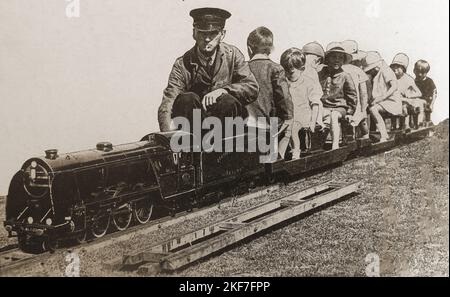 Das Bild der 30er Jahre von britischen Kindern, die eine Zugfahrt auf einem Miniatureisenbahnmotor des Typs King Arthur genießen. Stockfoto