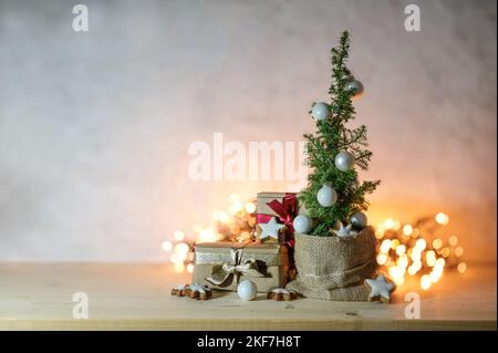 Alternativer platzsparender Weihnachtsbaum, kleine Topfkoniferpflanze, geschmückt mit Kugeln, Sternen und Geschenken vor verschwommenen Lichterketten, großer CO Stockfoto