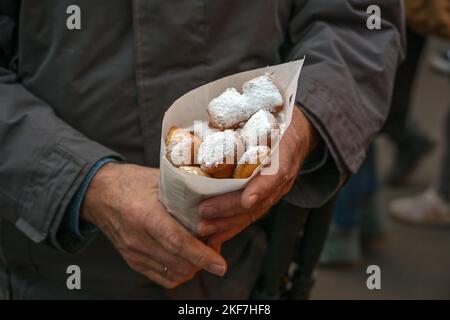 Mann, der einen Papiersack mit Mutzenmandeln hält, frittierten Mürbeteigteig mit Mandeln, die mit Puderzucker bedeckt sind, traditioneller deutscher Imbiss o Stockfoto