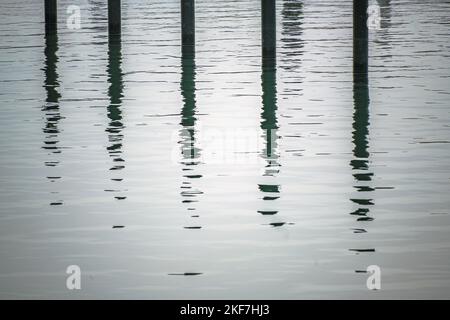 Schwarze Ankerhaufen oder Delfine mit Spiegelung im Wasser in einem leeren Jachthafen an der Ostsee an einem grauen Novembertag, abstraktes Bild, fast Stockfoto