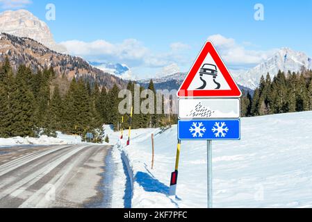 Rutschiges Straßenwarnschild an einem sonnigen Wintertag entlang einer Bergstraße Stockfoto