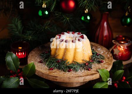 Gebüngelter Kuchen mit Zuckerzuckerung und Granatapfel in Weihnachtsstimmung. Stimmungsvolle Atmosphäre mit Kerzen und Dekoration. Silvester. Nachtisch genannt Stockfoto