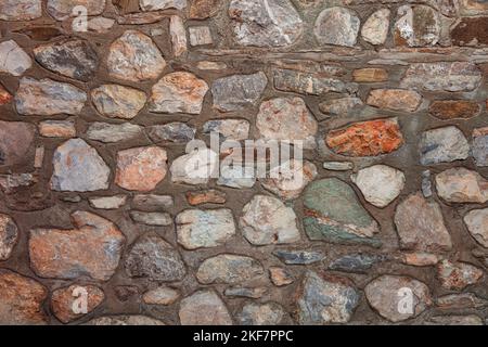 Steinwall Hintergrund mit starker Verwendung von Zement. Stonewall aus farbigen Steinen. Stockfoto