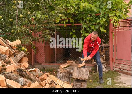 Ein Mann hackt Brennholz für den Winter, ein junger Mann spaltet ein Holz mit einer Axt. Teile des Holzes fliegen auseinander. Selektive Fokussierung. Stockfoto