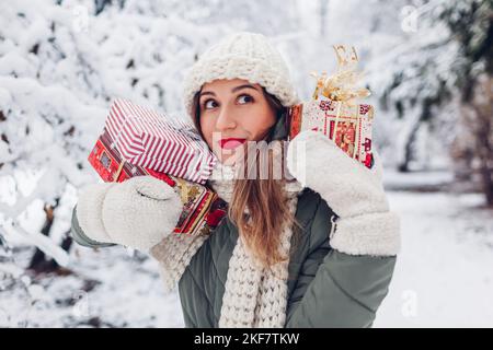 Junge Frau, die im verschneiten Winterpark im Freien eine Menge Weihnachtsgeschenkboxen trägt. Geschenke in Festpapier verpackt Stockfoto