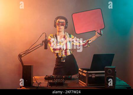 Disc Jockey Werbekarton Sprechblase im Studio, zeigt isolierte Textnachricht Karton. Junge dj-Performer mit Plakatwand-Mockup-Vorlage mit Coyspace, Plattenspielern aus Vinyl. Stockfoto