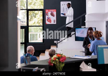 Medizinische Assistentin im Gespräch mit der Empfangsdame, die den Patiententermin während der Arbeit im Wartebereich des Krankenhauses bespricht. Menschen, die Check-up Besuch Beratung mit dem Arzt, Planung der Gesundheitsversorgung Behandlung Stockfoto