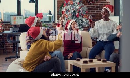 Multiethnisches Team von Mitarbeitern klirren Gläser mit Alkohol, um Weihnachtsfeiertage im Büro zu feiern. Die Menschen fühlen sich festlich und stoßen mit Wein auf die Weihnachtsfeier an. Stockfoto