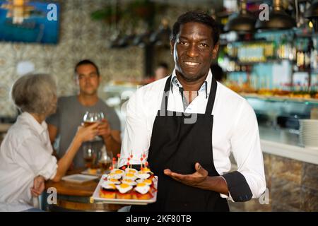 Blick auf den erwachsenen afrikanischen Mann, der in einem Pub Tapas hält Stockfoto