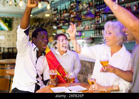 Begeisterte diverse Fußballfans mit der spanischen Flagge, die den Sieg mit einem Pint Bier in der Kneipe feierte Stockfoto