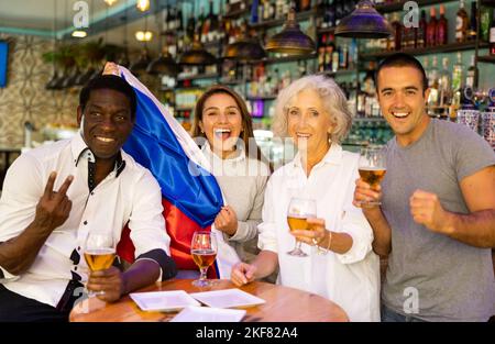 Fröhliche, vielfältige Fußballfans mit der russischen Flagge verbringen Zeit zusammen mit einem Pint Bier in der Kneipe Stockfoto