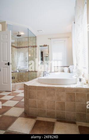 Badewanne mit braunem und braunem Keramiksockel und Glasdusche im Hauptbadezimmer im Obergeschoss im modernen Haus. Stockfoto