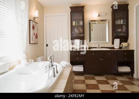 Badewanne mit braunem und braunem Keramiksockel und hölzernem Kosmetikbereich im Hauptbadezimmer im Obergeschoss im modernen Haus. Stockfoto