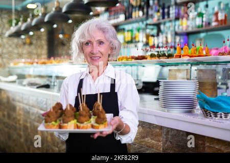 Blick auf die europäische ältere Frau, die an einer Bar Pinchos hält Stockfoto