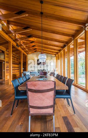 Esstisch aus Holz mit Ledersesseln, schwarzen Ledersesseln und Kupfer im industriellen Stil mit Hängeleuchten aus Milchglas. Stockfoto