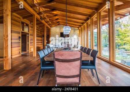 Esstisch aus Holz mit Ledersesseln, schwarzen Ledersesseln, Kupfer im industriellen Stil mit Hängeleuchten aus Milchglas im Esszimmer. Stockfoto