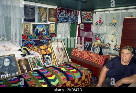 Ilfov County, Rumänien, ca. 2000. Frau in ihrem alten traditionellen Haus, mit einfachen Möbeln, handgefertigten Teppichen und einer Sammlung christlich-orthodoxer Ikonen. Stockfoto
