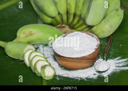 Bananenpulver auf Holzschüssel und rohe Banane - Bananenfrucht auf Blattgrund, Alternativmehl, hausgemachtes grünes Bananenmehl für Kräutermedizin Natu Stockfoto