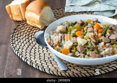 Nahaufnahme einer Schüssel mit hausgemachtem Rindfleisch- und Gersteneintopf, serviert mit Dinnerbrötchen. Stockfoto