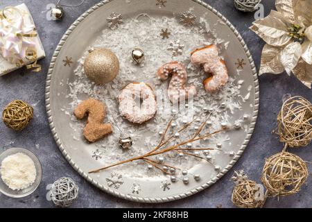 Eine silberne Platte mit 2023 gespritelten Donuts, umgeben von festlichen Dekorationen. Stockfoto